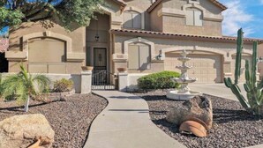A two-story house with a tiled roof, a front entrance with a door, and a small garden with a cactus and a fountain. - Wonderful 5-bedroom house in welcoming Gilbert (Gilbert)