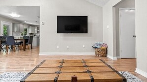 A living room with a mounted TV, a dining area, and a kitchen in the background. - Quaint 3-bedroom house with AC in charming Spring (Spring)