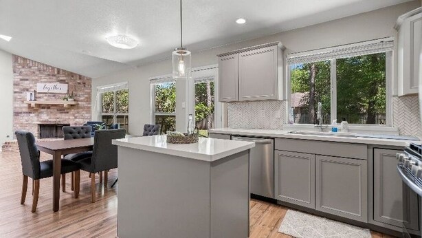 A modern kitchen with grey cabinets, a central island, and a dining area with dark chairs. - Quaint 3-bedroom house with AC in charming Spring (Spring)