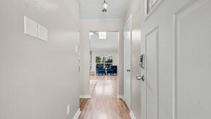 A hallway with a wooden floor, white walls, and a door on the right. - Quaint 3-bedroom house with AC in charming Spring (Spring)