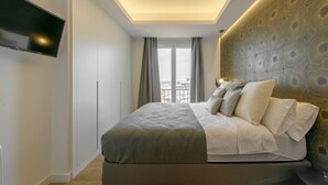 A modern bedroom with a large bed, a flat-screen TV mounted on the wall, and a view of the city through the window. - GRAN VIA capitals, LAS VEGAS (Madrid)
