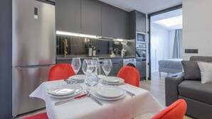 A modern kitchen with grey cabinets, a stainless steel refrigerator, and a dining area with a table set for four. - GRAN VIA capitals, LAS VEGAS (Madrid)