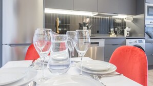 A modern kitchen with stainless steel appliances, a dining table set with white plates and glasses, and a red chair. - GRAN VIA capitals, LAS VEGAS (Madrid)