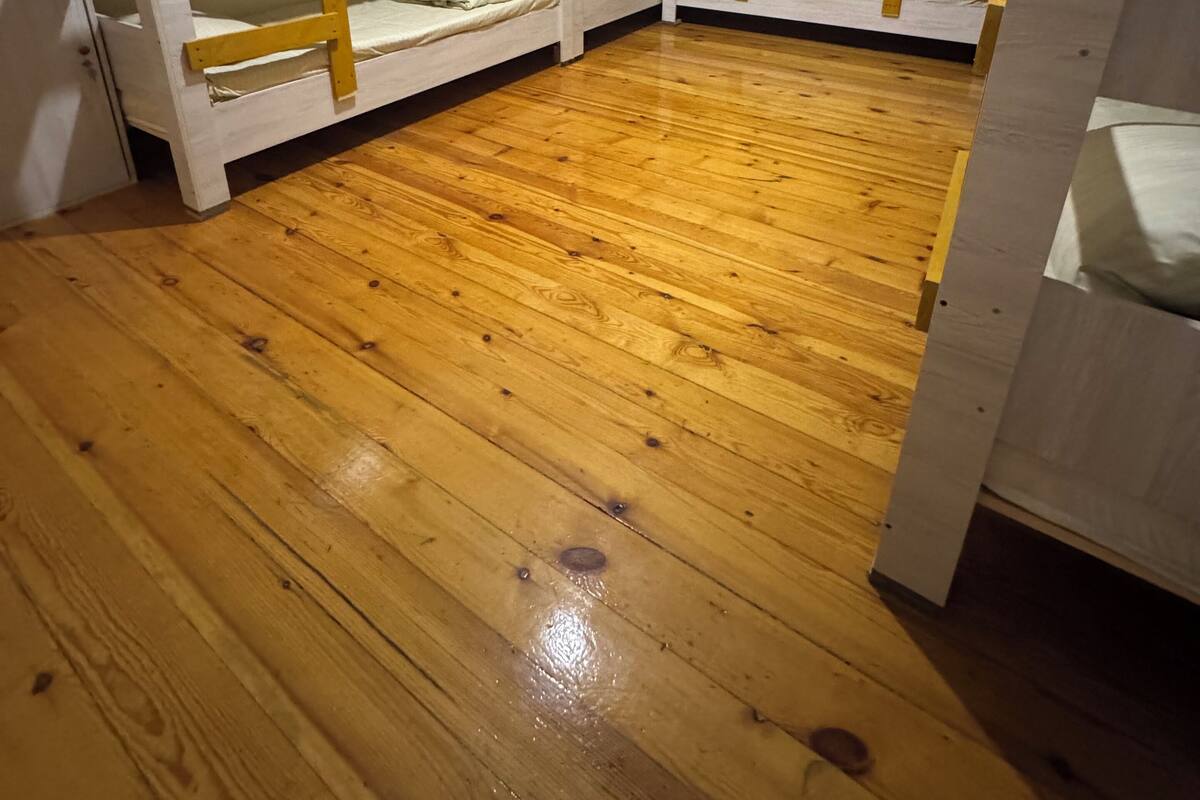 Quarto com três beliches, piso de madeira e paredes brancas.