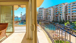 A balcony with a view of a swimming pool and adjacent hotel buildings. - Premium Ocean Views & Unbeatable Convenience: Villa La Estancia 1303 (Cabo San Lucas)