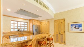 A kitchen with a large island, wooden cabinets, and a stainless steel refrigerator. - Premium Ocean Views & Unbeatable Convenience: Villa La Estancia 1303 (Cabo San Lucas)