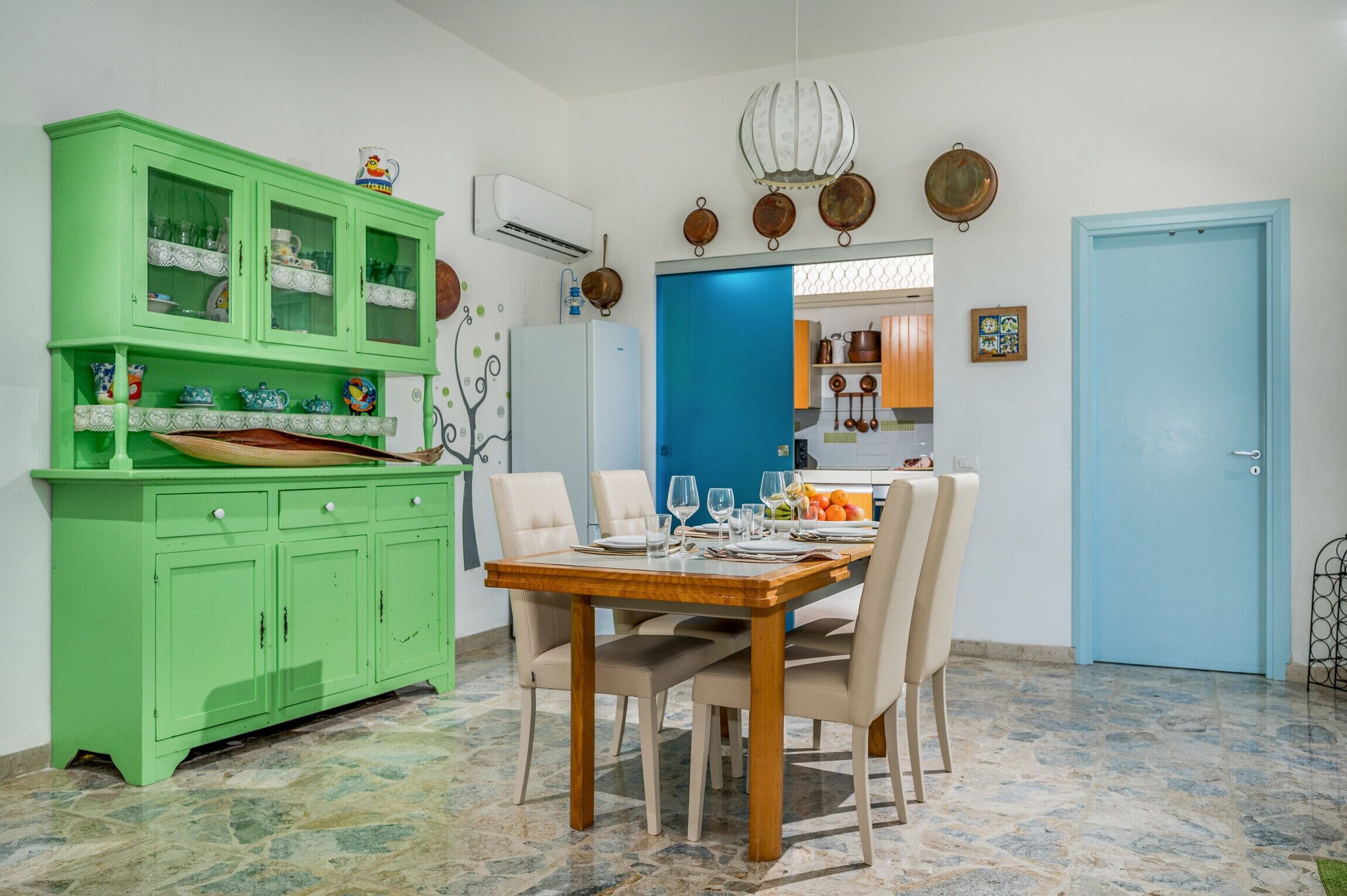 A dining area with a green cabinet, a blue door, and a tiled floor.