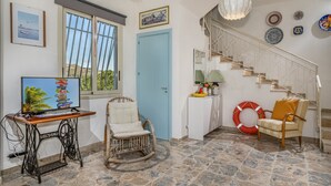A room with a wooden table, a rocking chair, a television, a blue door, a staircase, and a wall with decorative plates. - Villa Le Terrazze Blu (Castellammare del Golfo)