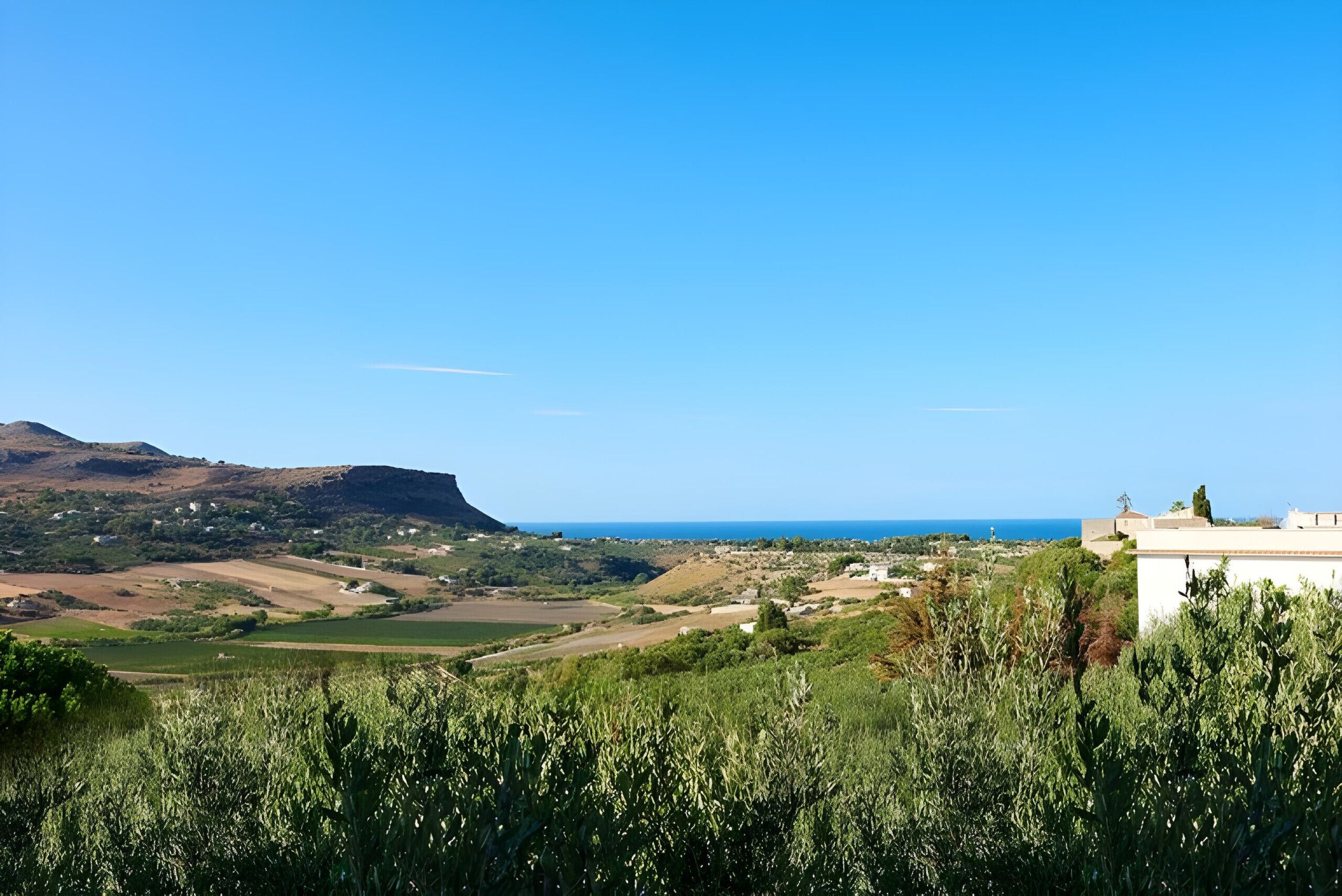 A coastal landscape with a view of the sea, rolling hills, and scattered buildings.