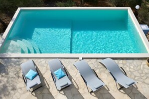 A rectangular swimming pool with clear blue water, surrounded by a stone deck. There are four lounge chairs with blue cushions aligned along the pool's edge. - Villa Le Terrazze Blu (Castellammare del Golfo)