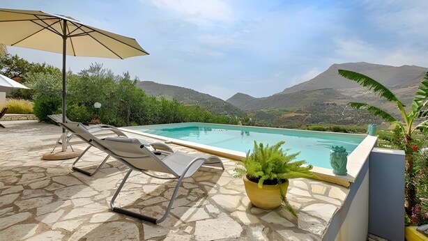 A pool with lounge chairs and an umbrella, surrounded by greenery and mountains. - Villa Le Terrazze Blu (Castellammare del Golfo)