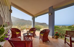A balcony with wicker chairs, a small table, and a potted plant. - Villa Le Terrazze Blu (Castellammare del Golfo)