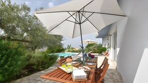 An outdoor patio with a table and chairs, a large umbrella, and a pool in the background. - Villa Le Terrazze Blu (Castellammare del Golfo)