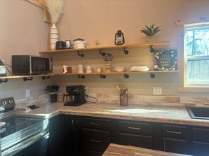 Una cocina con microondas, cafetera y varios frascos de almacenamiento en estantes.