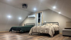 A bedroom with two beds, a window with curtains, an air conditioning unit, and a ceiling light fixture.