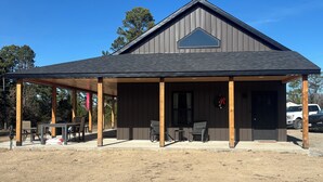 A covered outdoor seating area with tables and chairs, a building with a dark roof and wooden pillars, and a clear blue sky in the background.