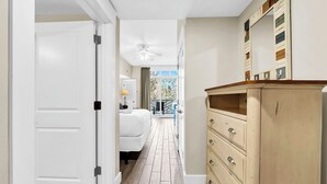Un couloir étroit doté d’un plancher en bois, une porte blanche sur la gauche et une commode beige avec des tiroirs sur la droite.
