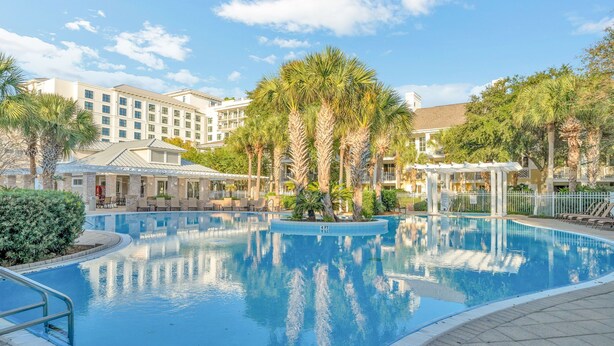 Une piscine entourée de palmiers et un bâtiment d’hôtel.