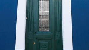 Eine grüne Tür mit kleinem Fenster und einem dekorativen Feld, in einer weiß-blauen Gebäudefassade.