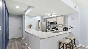 Una cucina moderna con mobili bianchi, un'isola centrale e due sgabelli da bar.