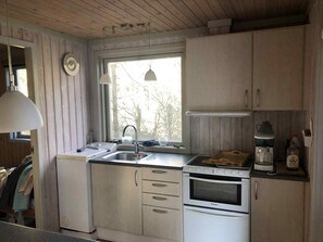Uma cozinha com armários de madeira, pia, fogão e janela com vista para árvores.