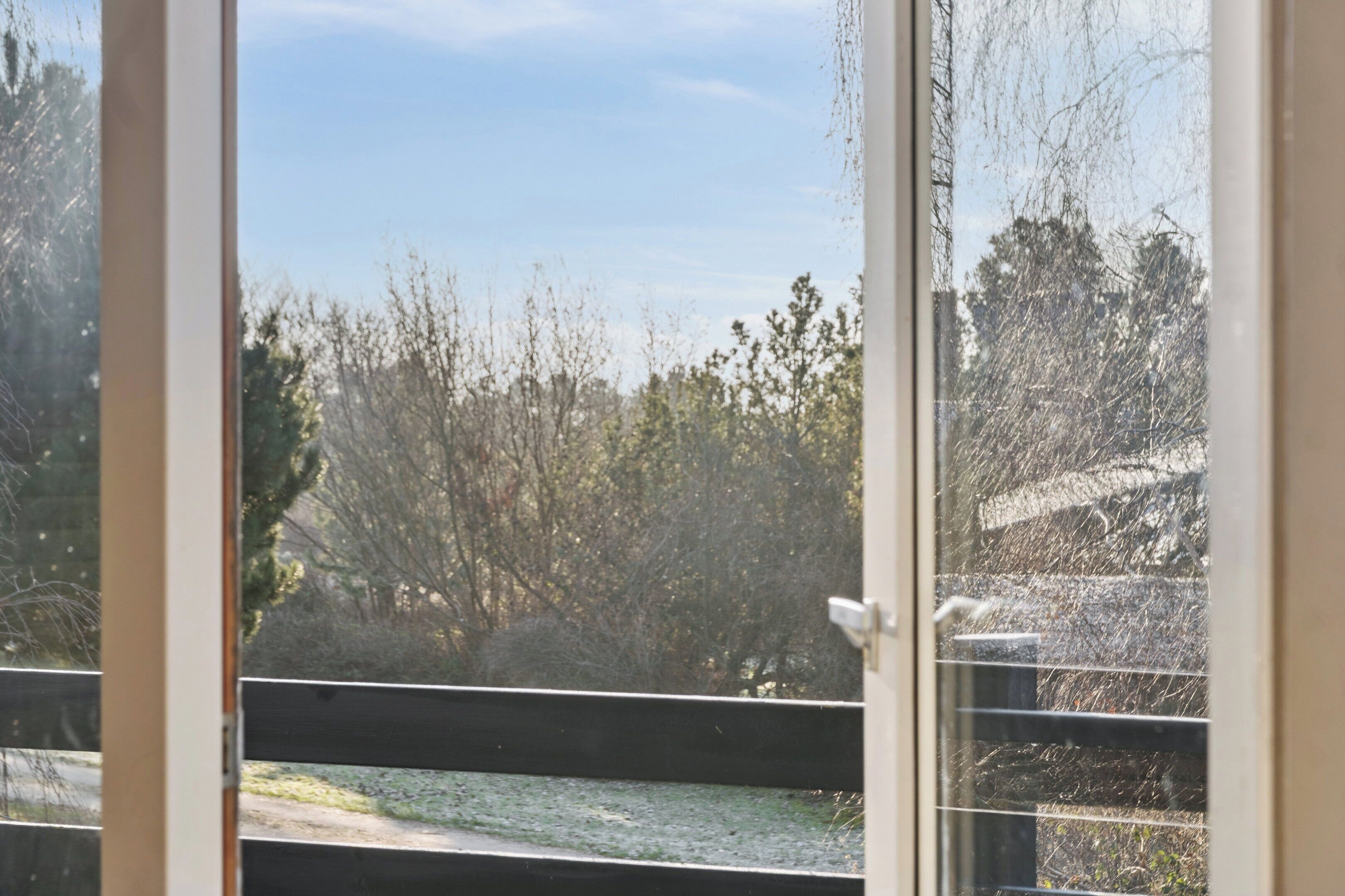 A view through a window with a metal railing, trees, and a clear sky.