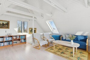 Ein geräumiger Loft mit hohen Decken, Holzregalen, einem blauen Sofa und einem Esstisch.