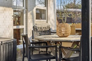 En udendørs terrasse med et rundt bord, sorte metalstole og en fletkurv.