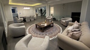 Un salon spacieux avec une table basse ronde, des sièges confortables, un lustre et un escalier menant à un niveau supérieur.
