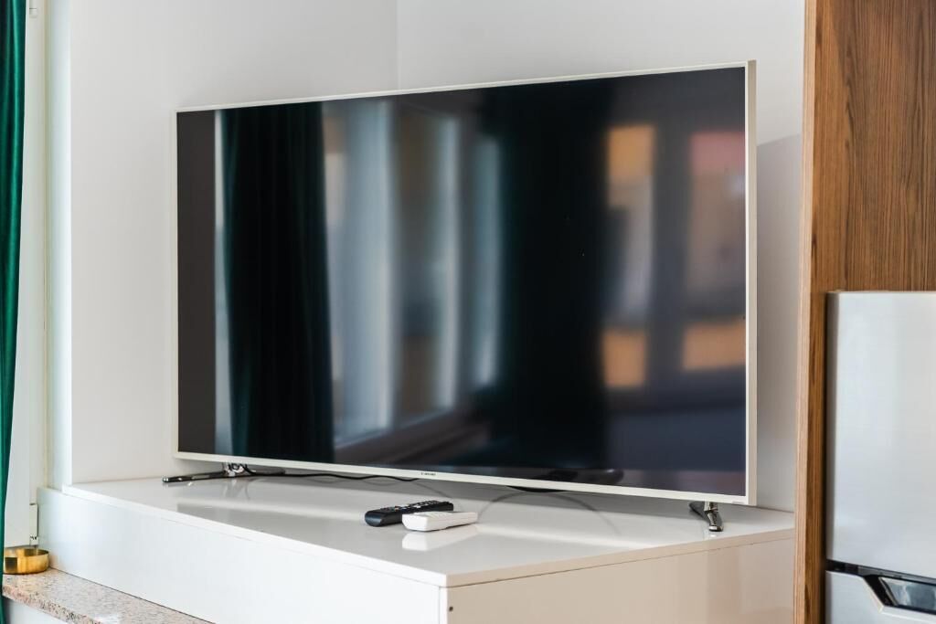 Ein Flachbildfernseher an einer weißen Kommode, mit Fernbedienung darauf.
