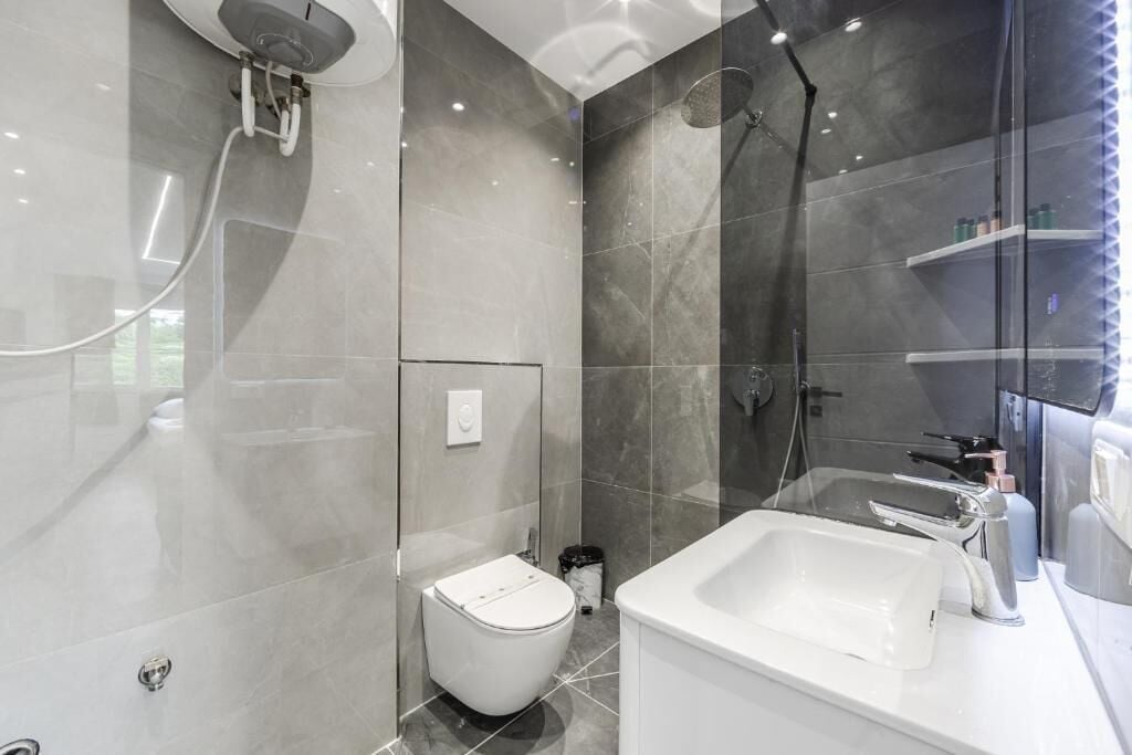 Ein modernes Badezimmer mit einer Duschkabine aus Glas, einer weißen Toilette und einem großen Waschbecken mit Spiegel.