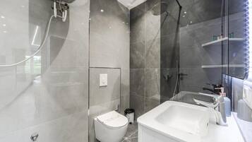A modern bathroom with a glass shower enclosure, a white toilet, and a large sink with a mirror.