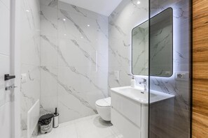 Ein modernes Badezimmer mit Marmorfliesen, einem weißen Waschbecken und einem großen Spiegel.