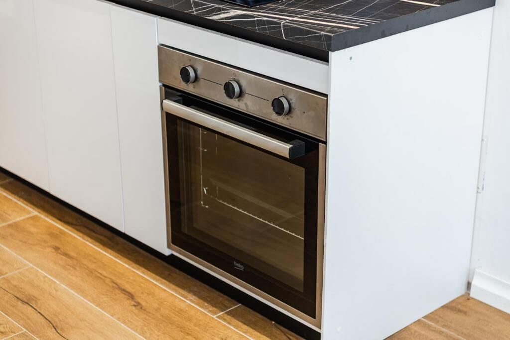 A kitchen with white cabinets, a stainless steel oven, and a black countertop.