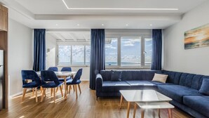 Una sala de estar moderna con un sofá, una mesa de centro y sillas. Hay un ventanal con cortinas y un cuadro en la pared.