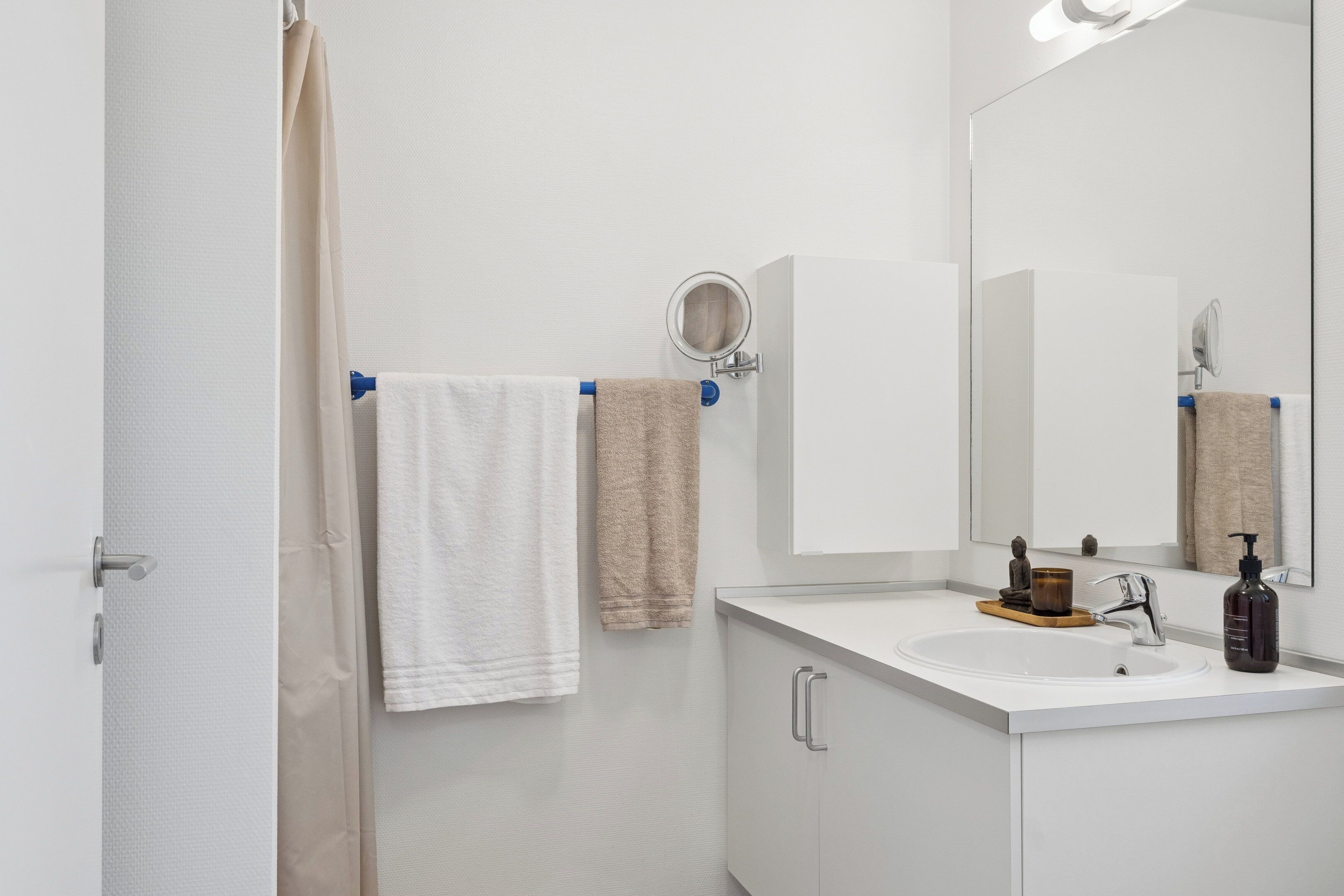 A bathroom with a white sink, a mirror, a towel rack with two towels, and a bottle of shampoo.