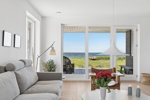 A modern living room with a large sliding glass door leading to an outdoor patio with a view of the sea. - Magnificent seaside villa with stunning views (Hundested)