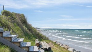 Eine Küstenlandschaft mit einer Holztreppe, die zum Strand führt, umgeben von Felsen und Vegetation.