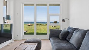 Ein Wohnzimmer mit großem Fenster, einem grauen Sofa, einem Fernseher und einer Lampe.