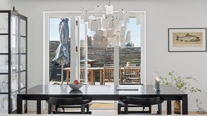 Ein moderner Essbereich mit einem schwarzen Tisch, zwei Stühlen, einem Glaskabinett und Blick durch eine Glastür auf einen Außenbereich mit Tisch und Stühlen.