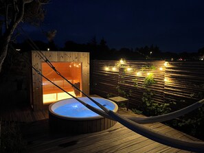 A wooden hot tub on a deck with a hammock, surrounded by a wooden fence with string lights. - Magnificent seaside villa with stunning views (Hundested)