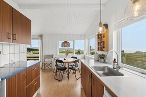 A modern kitchen with wooden cabinets, a dining table with chairs, a large window, and a view of the outdoors. - Charming holiday home with Baltic Sea views (Allinge)