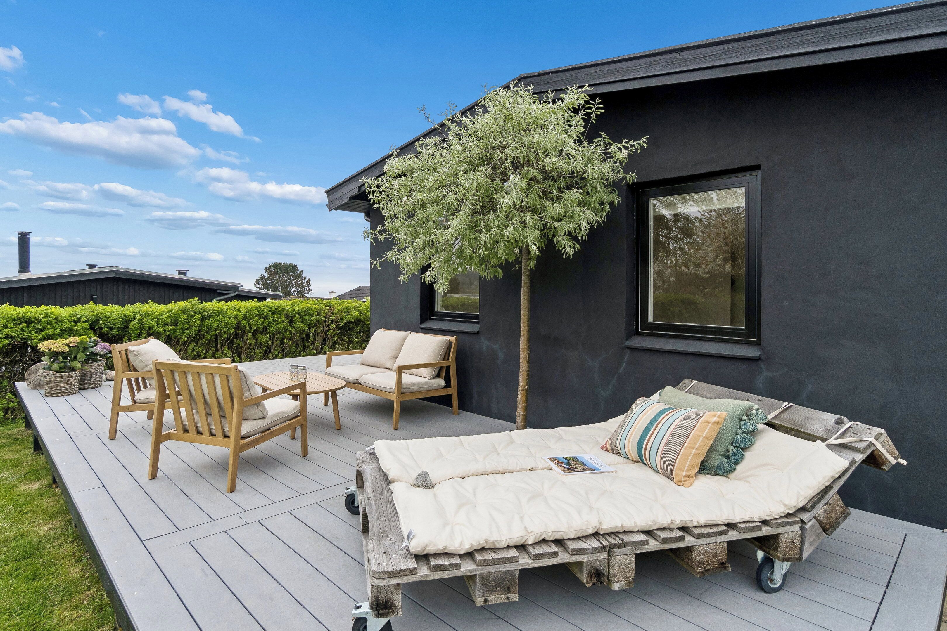 A deck with wooden furniture, a cushioned bench, and a tree.