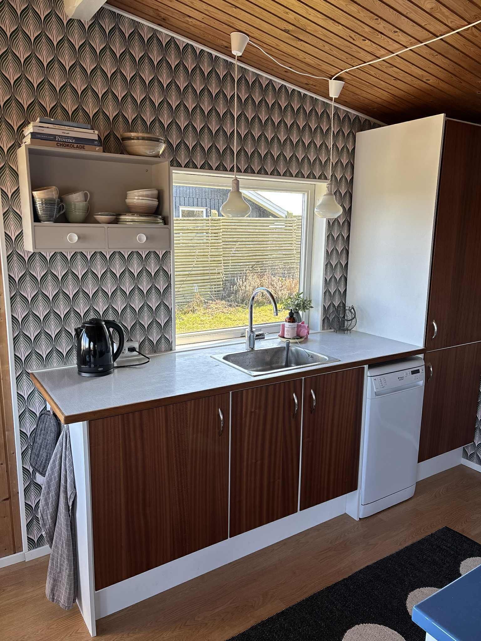 A kitchen with wooden cabinets, a built-in dishwasher, a window with a view, and a patterned backsplash.