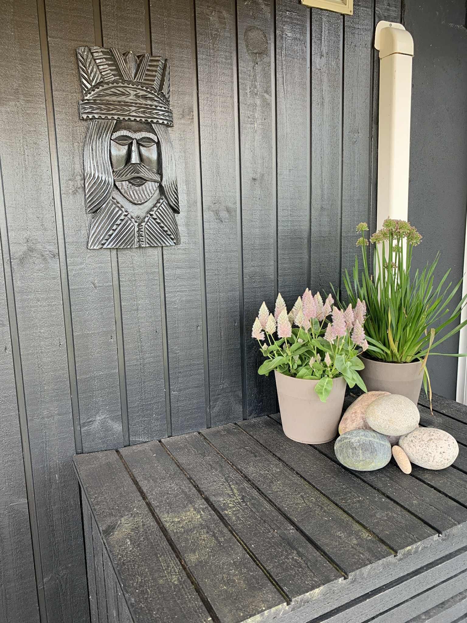 Eine Holzwand mit einer verzierten Metallrelief, zwei Blumentöpfen und einer Bank.