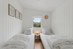 A bedroom with two beds, a small table with a lamp, a window, and framed botanical prints on the wall. - Charming holiday home with Baltic Sea views (Allinge)
