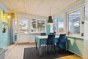 Un área de comedor con una mesa, sillas, una lámpara colgante y vistas a través del ventanal.
