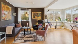 Een moderne woonkamer met een bank, fauteuils, een salontafel en een groot raam met uitzicht.