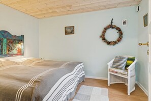 A bedroom with a bed, a chair, a wall-mounted wreath, and a painting. - Relaxing holiday home close to the sea (Korsør)