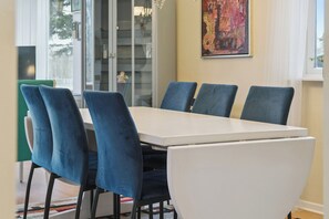 A dining area with a white table and blue chairs, a glass cabinet, and a painting on the wall. - Relaxing holiday home close to the sea (Korsør)